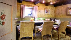 Een rustiek houten interieur met rieten stoelen, een tafel met een bloevas en een silhouet van een hert op de muur.