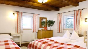 Een slaapkamer met twee bedden, een houten dressoir, een spiegel en een raam met gordijnen.