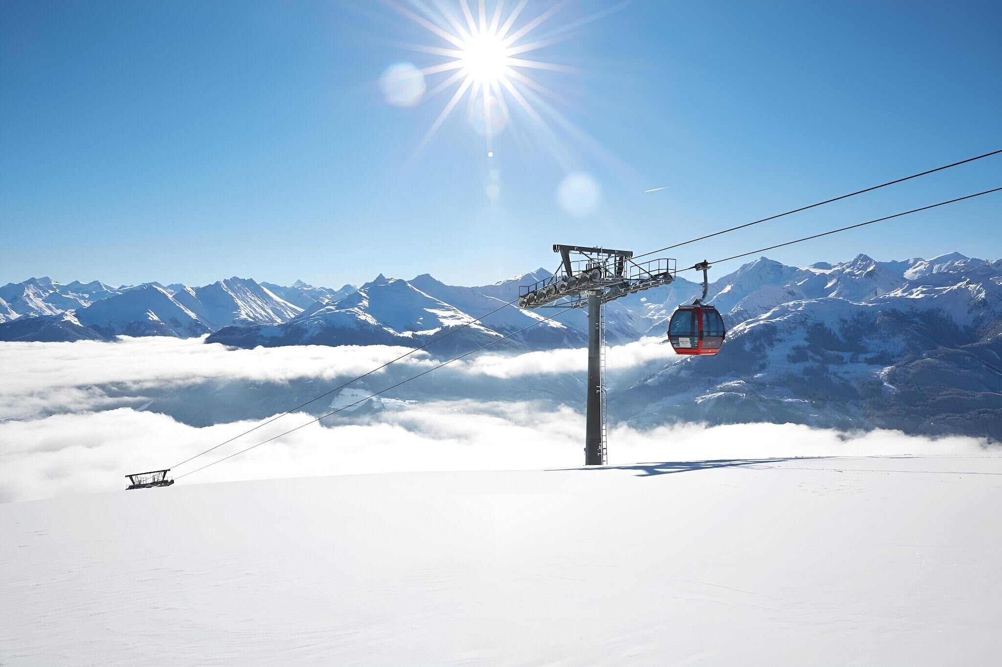 Eine Seilbahn in einer verschneiten Berglandschaft bei klarem Himmel und strahlender Sonne.