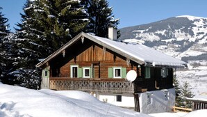 Een houten chalet met een balkon, omringd door met sneeuw bedekte bomen en bergen op de achtergrond.