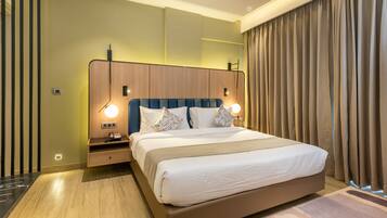 A modern hotel room with a large bed, wooden headboard, bedside lamps, and a view of the city through large windows.