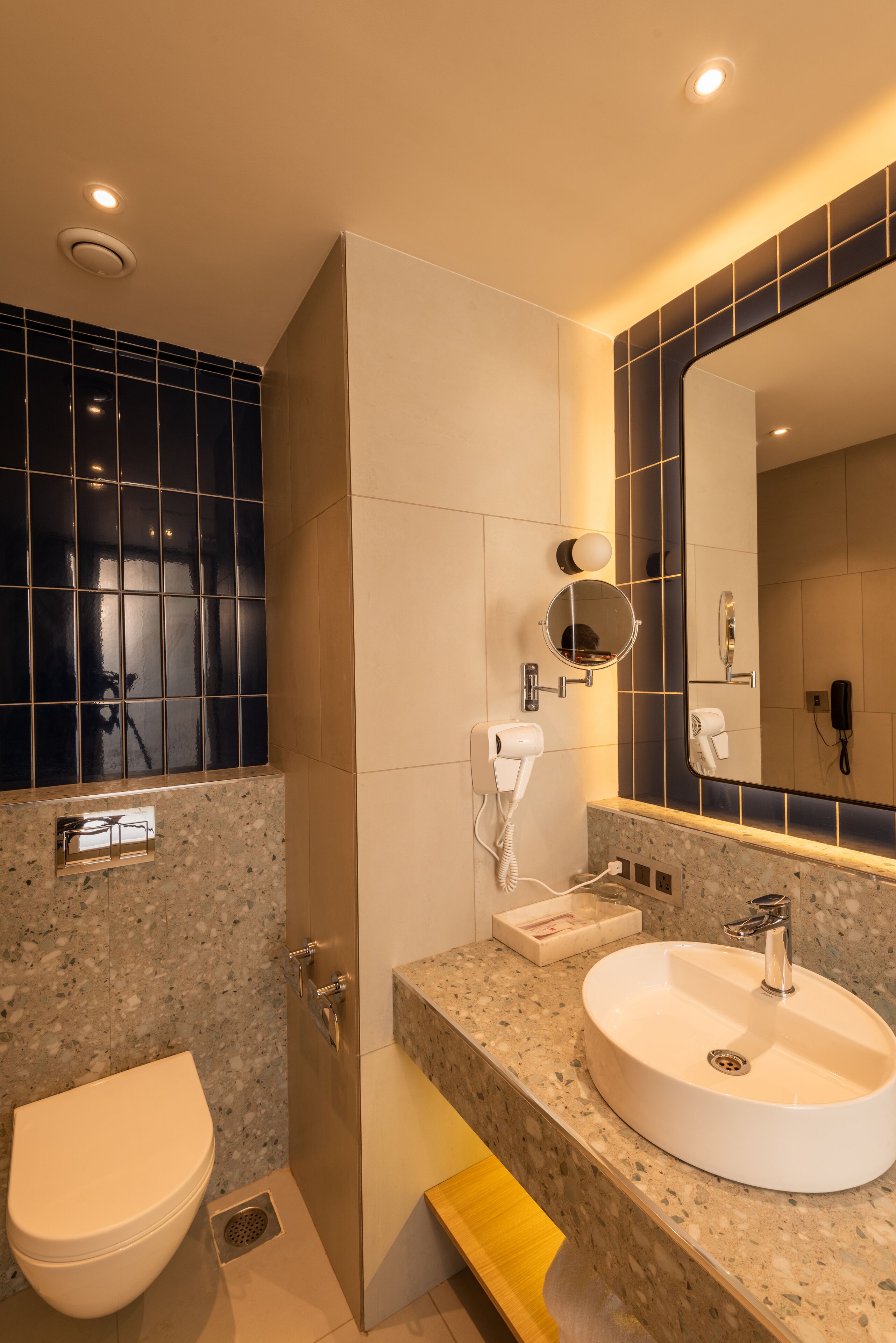 Une salle de bain avec un lavabo blanc, un miroir, un sèche-cheveux et des toilettes.
