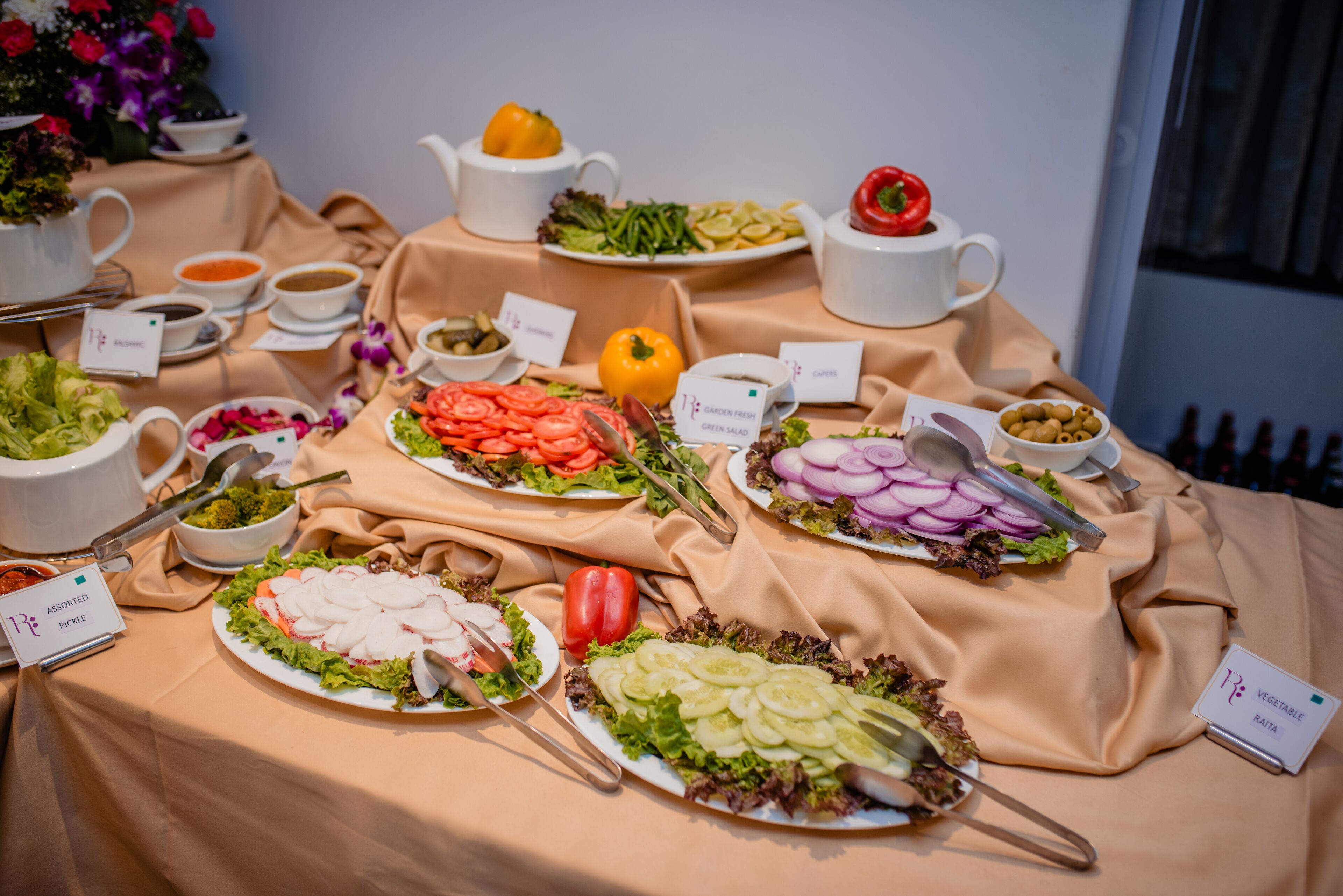 Une table de buffet proposant diverses salades et sauces, notamment une salade composée d’ingrédients frais du jardin et une salade de légumes.