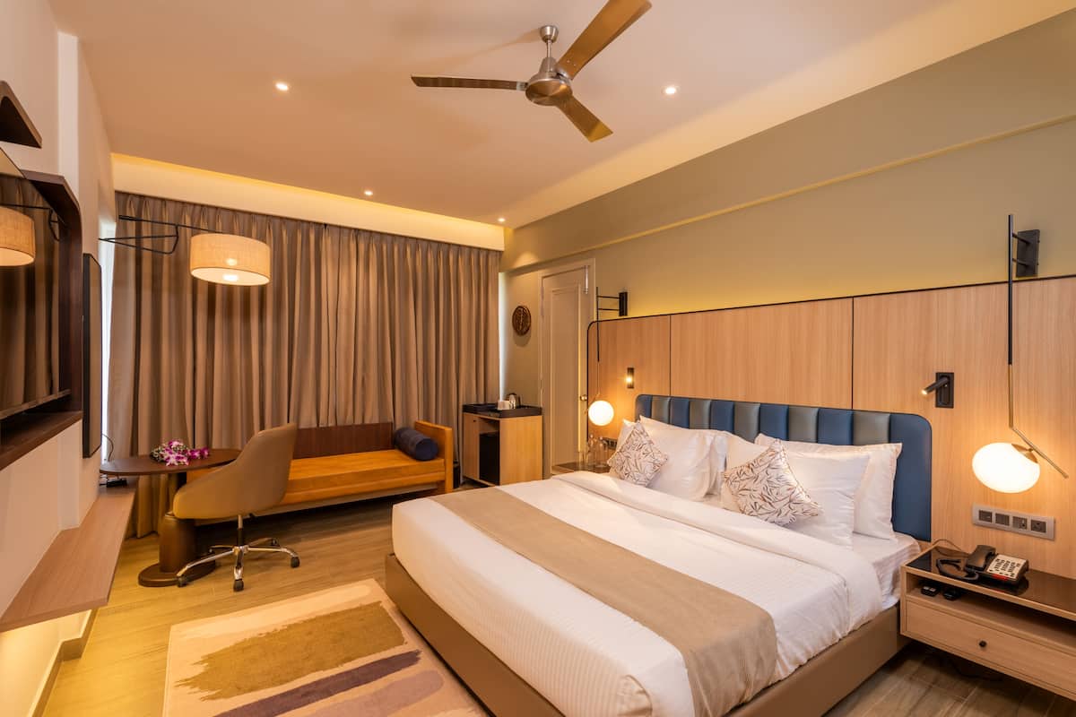 Ein modernes Hotelzimmer mit einem großen Bett, einem Schreibtisch, einem Sessel und einem Deckenventilator.