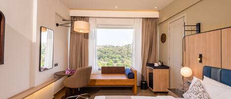 A modern hotel room with a bed, desk, chair, and a view of the outdoors.
