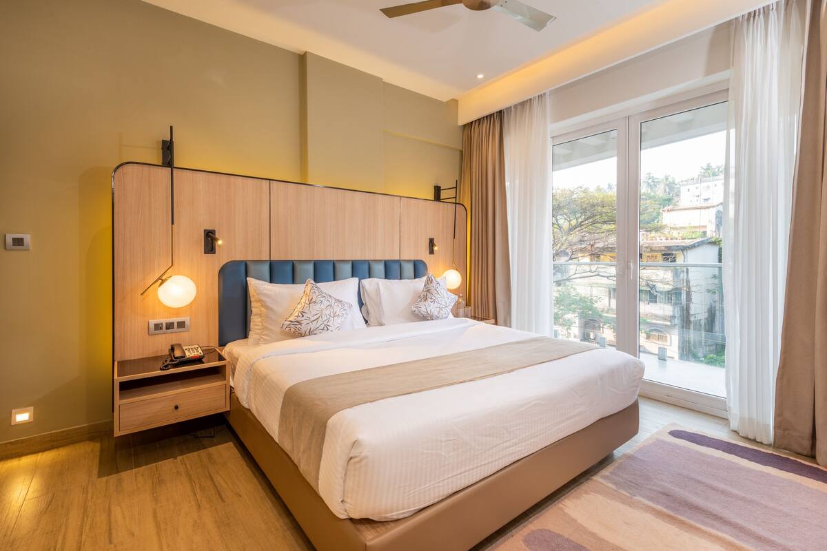 Ein modernes Hotelzimmer mit einem großen Bett, Nachttischen, einem Telefon und Blick auf die Stadt durch ein großes Fenster.