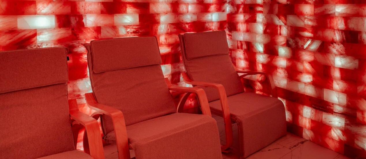 Three red chairs with wooden armrests in a room with a red and white patterned wall.
