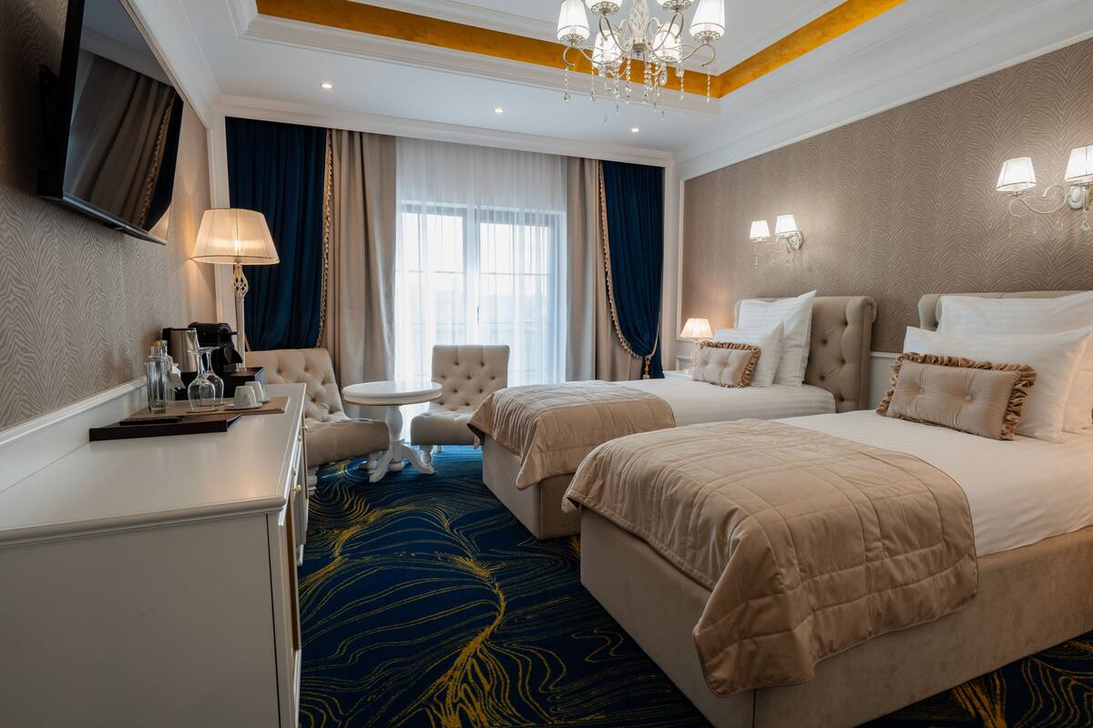 Une chambre d’hôtel avec deux lits, un bureau, une chaise, une télévision et un lustre.