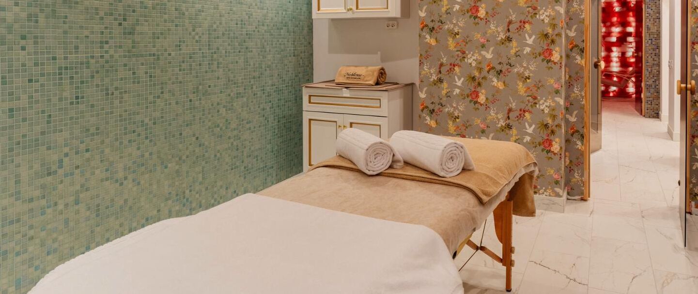 A spa room with a massage table, a small cabinet, and a floral curtain.