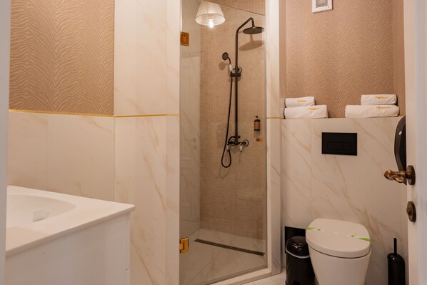 Un baño con ducha envuelta en vidrio, un lavamanos blanco y un inodoro con un candado verde.