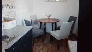 Ett kompakt kök med en matplats, bestående av ett litet runt bord och två stolar, en inbyggd ugn och en mikrovågsugn.