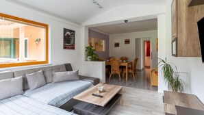 A modern living room with a sofa, a coffee table, and a dining area with a table and chairs. - Apartment Neukirchen near Ski Slopes (Neukirchen am Großvenediger)