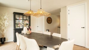A dining area with a dark wooden table, white chairs, and a black cabinet with glass doors. - Family Getaway in Texel (De Koog)
