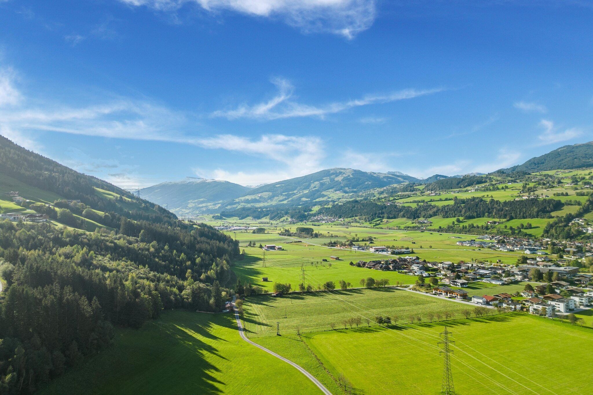 A rural landscape with a small village, green fields, and mountains in the background.