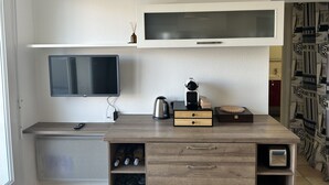 Ein modernes Wohnzimmer mit Flachbildfernseher, einer Holzvitrine mit Weinflaschen, einer Kaffeemaschine und einem dekorativen Gegenstand auf der Arbeitsfläche.
