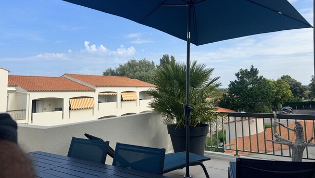Ein Balkon mit blauem Sonnenschirm, einem Blumentopf und Blick auf Gebäude mit roten Ziegeldächern.
