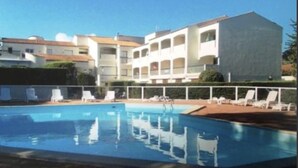 Ein Pool mit Liegestühlen und ein Gebäude mit mehreren Balkonen im Hintergrund.