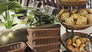 A buffet setup with various breads and pastries in wicker baskets, set in a spacious dining area with tables and chairs. - Gut am See Hotel & Restaurant  (Görlitz)