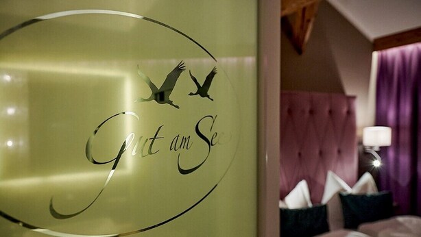 A room with a bed, a tufted headboard, and a wall with a circular logo featuring birds and the text "Get am Se". - Gut am See Hotel & Restaurant  (Görlitz)