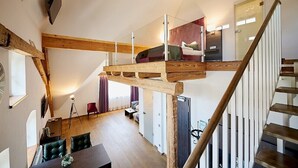 A loft-style bedroom with a glass ceiling, wooden beams, a staircase, and a view of the living area below. - Gut am See Hotel & Restaurant  (Görlitz)