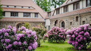 A courtyard with a stone building, surrounded by lush greenery and flowering shrubs. - Gut am See Hotel & Restaurant  (Görlitz)