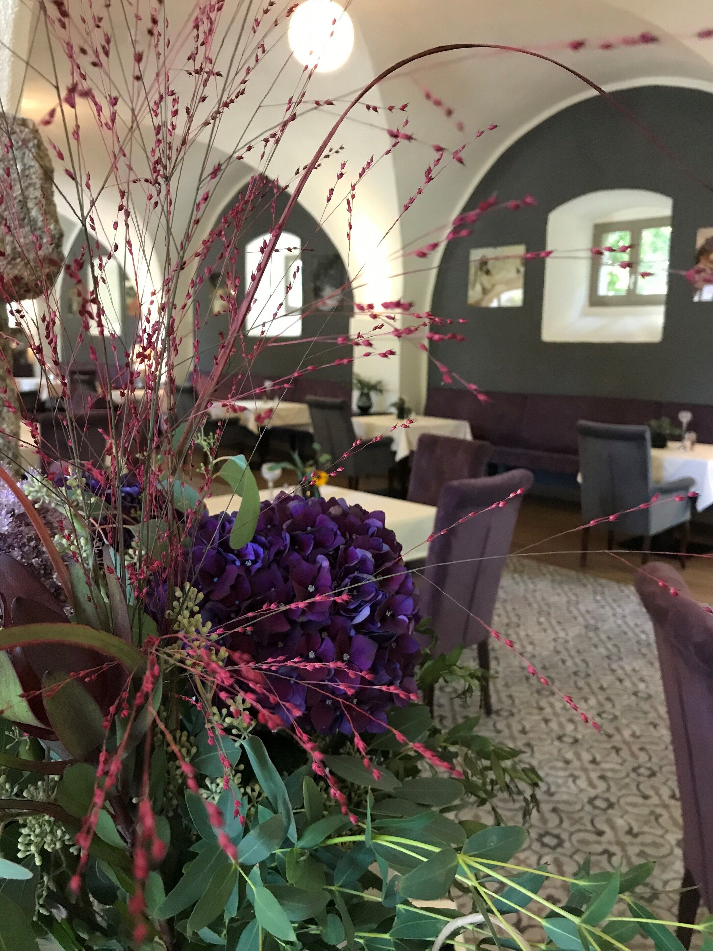 Un área de comedor con mesas y sillas, una decoración vegetal y una alfombra estampada.