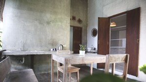 A rustic kitchen with a concrete countertop, wooden table, and chairs. There is a potted plant on the table. - Baannoi Nornmuan Homestay Chiang Mai (Chiang Mai)