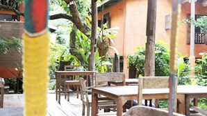 An outdoor patio with wooden tables and chairs, surrounded by lush greenery and a building with orange walls. - Baannoi Nornmuan Homestay Chiang Mai (Chiang Mai)