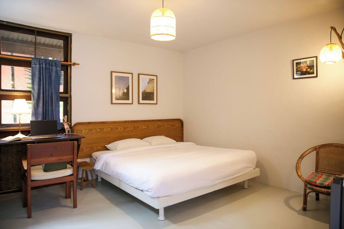 A bedroom with a wooden bed, a desk with a chair, and two framed pictures on the wall.