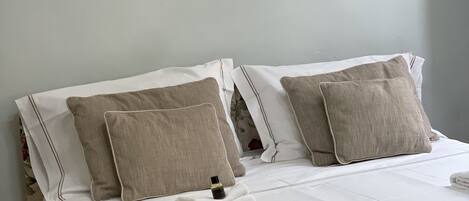 A neatly made bed with white linens, beige pillows, and a beige throw blanket.