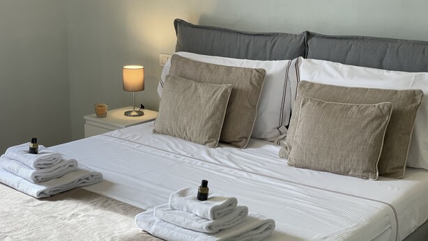 Een opgemaakt bed met witte lakens, twee kussens en gevouwen handdoeken.