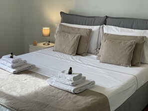 Una cama bien hecha con sábanas blancas, dos almohadas y toallas dobladas.