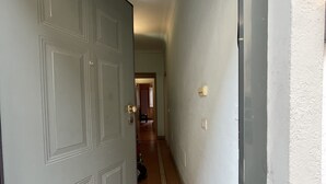 Een gang met een gesloten deur, een betegelde vloer en een lichtschakelaar aan de muur.