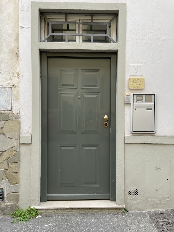 Una puerta verde oscuro con cerradura electrónica, una pequeña ventana encima y una caja de servicios a la derecha.