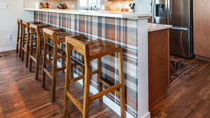 A modern kitchen with wooden cabinets, a stainless steel refrigerator, and a bar area with wooden stools. - Summer camp is here at Cle Elum Cabin! Featuring a private hot tub, shuffleboard, games galore, fully stocked kitchen and much more! (Cle Elum)