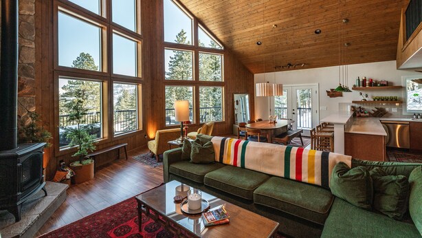 A spacious living room with a fireplace, large windows, a cozy sofa, and a kitchen area. - Summer camp is here at Cle Elum Cabin! Featuring a private hot tub, shuffleboard, games galore, fully stocked kitchen and much more! (Cle Elum)