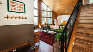 A spacious living area with a high ceiling, wooden beams, a staircase, and a large window. - Summer camp is here at Cle Elum Cabin! Featuring a private hot tub, shuffleboard, games galore, fully stocked kitchen and much more! (Cle Elum)