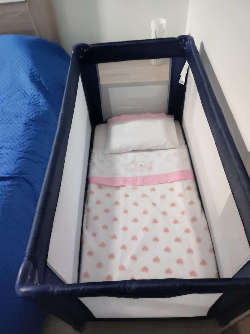 A crib with a white mattress and pink heart-patterned bedding, positioned against a blue wall.