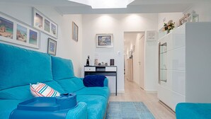 A modern living room with a teal sofa, a small side table, and a kitchen area in the background.