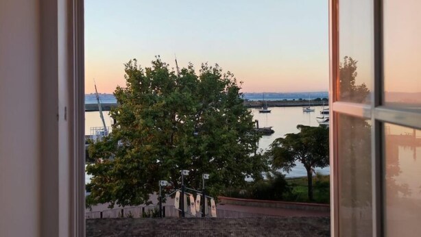 A room with a large window overlooking a body of water, trees, and a distant bridge.