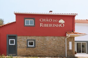En byggnad med en röd fasad och en sockel av sten, med texten ”CHÃO DO RIBEIRINHO”.