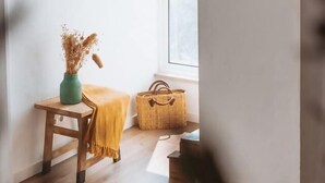 Une pièce avec un plancher en bois, une petite table sur laquelle est posé un vase, une chaise et un plaid jaune. Il y a une fenêtre donnant sur l’extérieur.