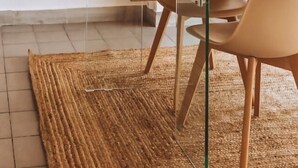 Un coin repas avec une table en bois, des chaises de couleur beige, un tapis tissé et des œuvres d’art encadrées accrochées aux murs.