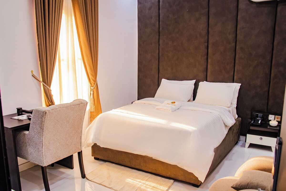 Una habitación estándar con cama, mesita de noche, silla y tocador.
