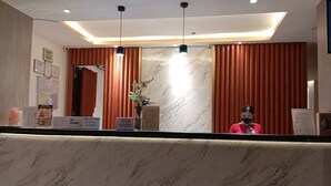 A hotel reception area with a marble counter, a receptionist, and a modern ceiling design. - Mc Hotel Fairview (Quezon City)