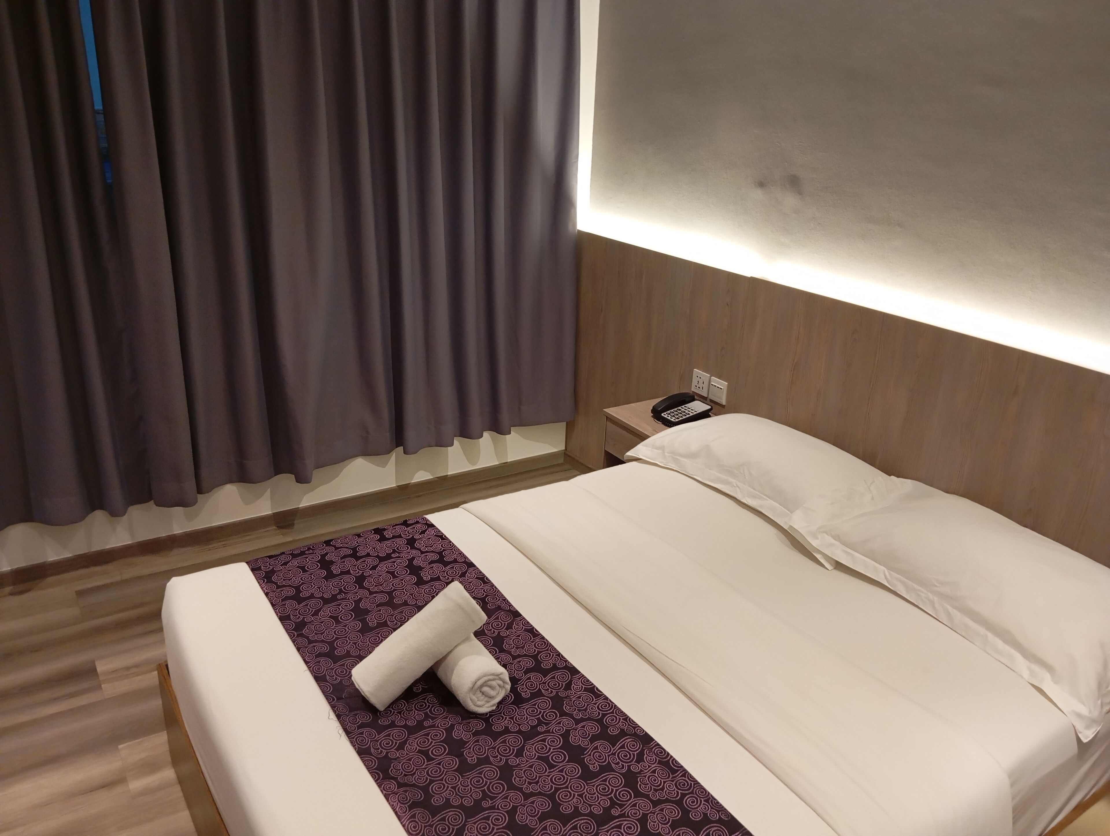 Et hotelværelse med en pænt redt seng, en telefon ved sengebordet og en lampe på væggen.
