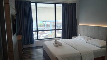 Une chambre d’hôtel avec un grand lit, un téléviseur fixé au mur et une vue sur la ville grâce à de grandes fenêtres.