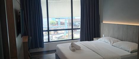 A hotel room with a large bed, a TV mounted on the wall, and a view of the city through large windows.