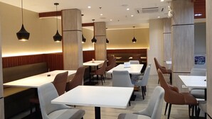 A modern restaurant interior with multiple tables and booths, recessed ceiling lighting, and wooden accents. - Mc Hotel Fairview (Quezon City)