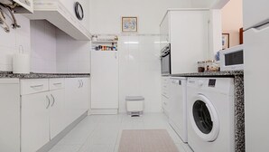 A compact kitchen with white cabinets, a built-in washing machine, and a small trash bin.